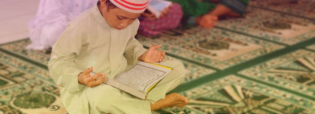 An image of a young boy meditating on scripture with the holy book open in his lap.