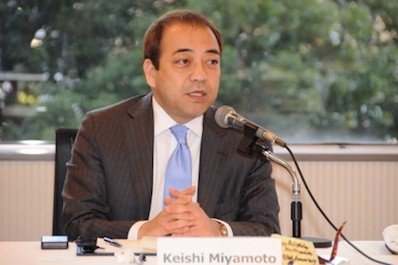 An image of Keishi Miyamoto as he gives a speech outdoors, sat behind a table.