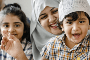 An image of a Muslim family with two children playfully interacting with the camera.