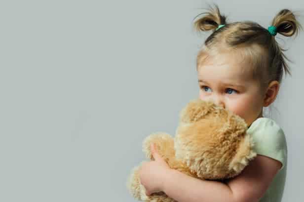 A little girl hugging a stuffed teddy bear.
