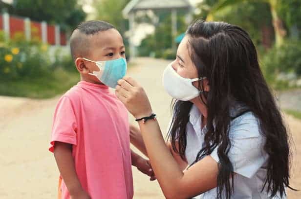 An older woman helping put on a surgical mask for a little boy.